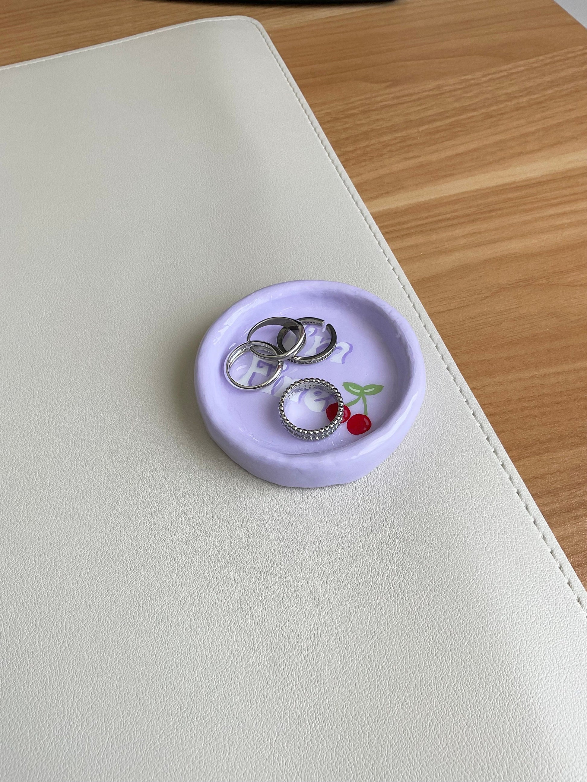 This cute tray dish has so many fun purposes. You can use this to hold your jewelry, simply use as a decor piece in your room or on your desk, or even as a mini coaster for a small can. This design is a light purple base, features the verbiage "I'm Fine" and has cherries painted on.