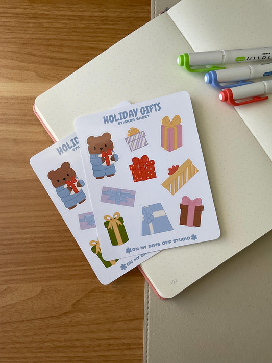 Holiday gifts sticker sheet front, featuring 1 illustration of a cute bear wearing winter sweater holding a present. Also, it includes 8 colorful gifts or present boxes. 